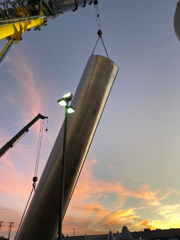 Crane lifting a stainless tank into place at sunset